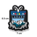 Magnet with 'Ladakh' design featuring mountains, leopards, and colorful flags on a black border.