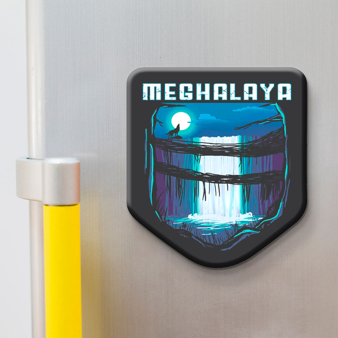 Fridge magnet with a design of a waterfall and 'MEGHALAYA' text on a metallic surface.