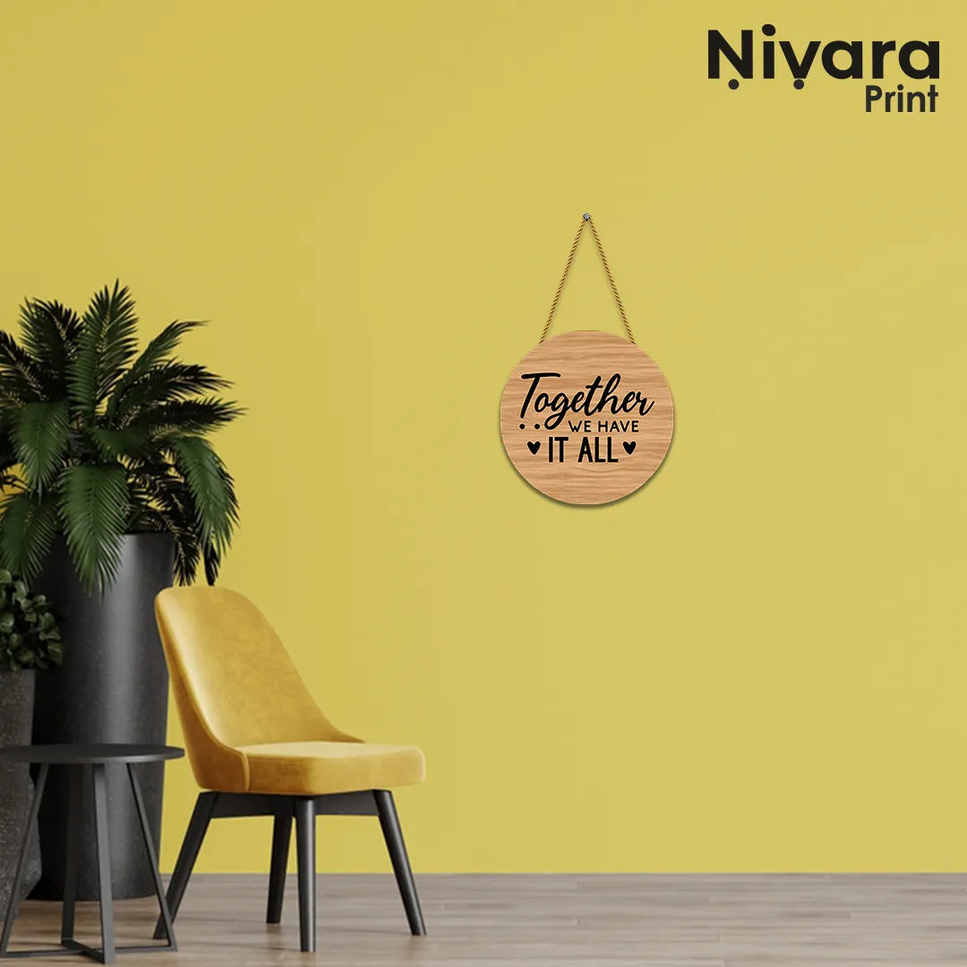 Round wooden sign with 'Together we have it all' text on a yellow wall with a chair and plant.
